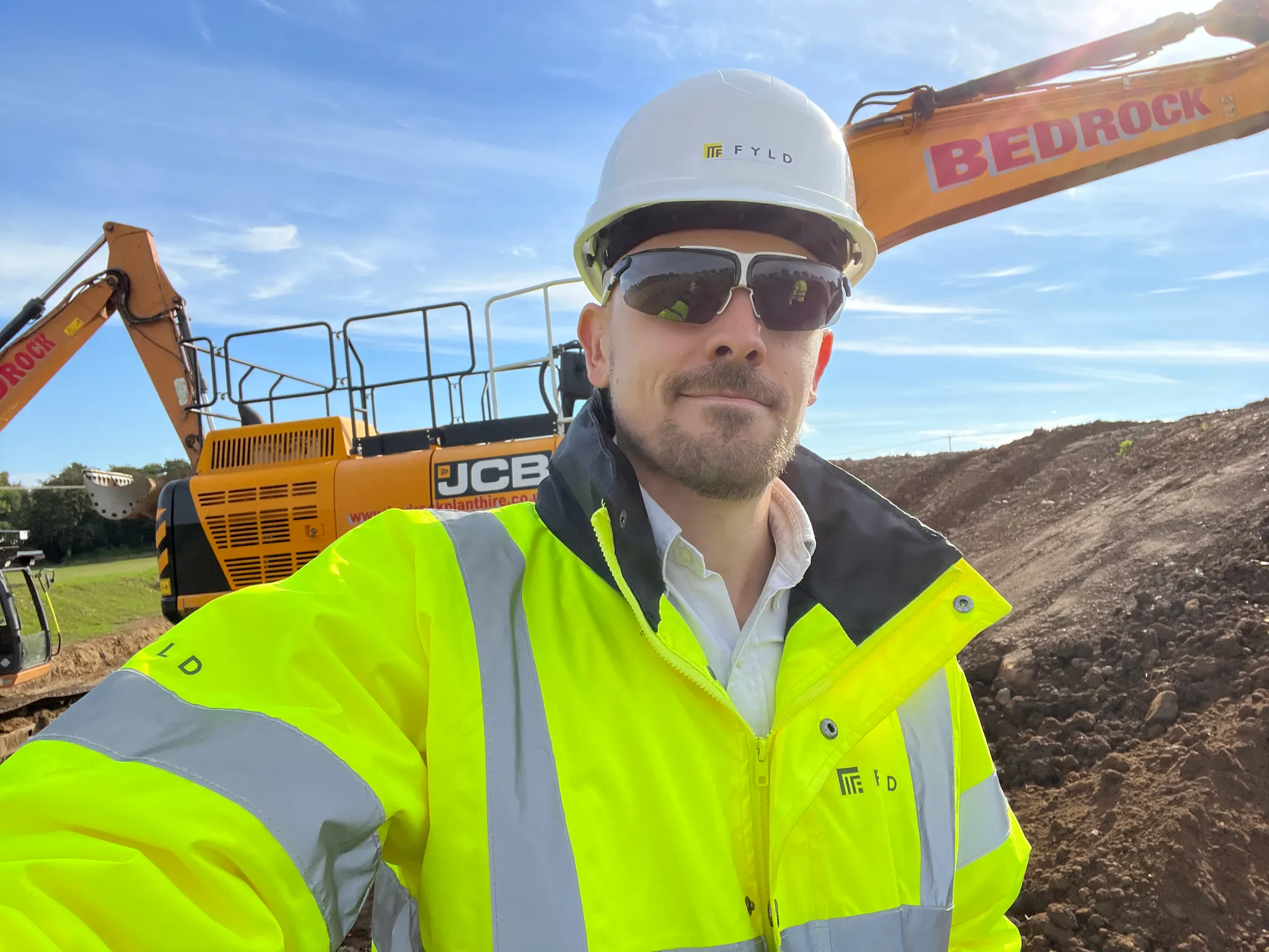 John Haynes on a utility worksite in FYLD-branded PPE, with construction excavators behind