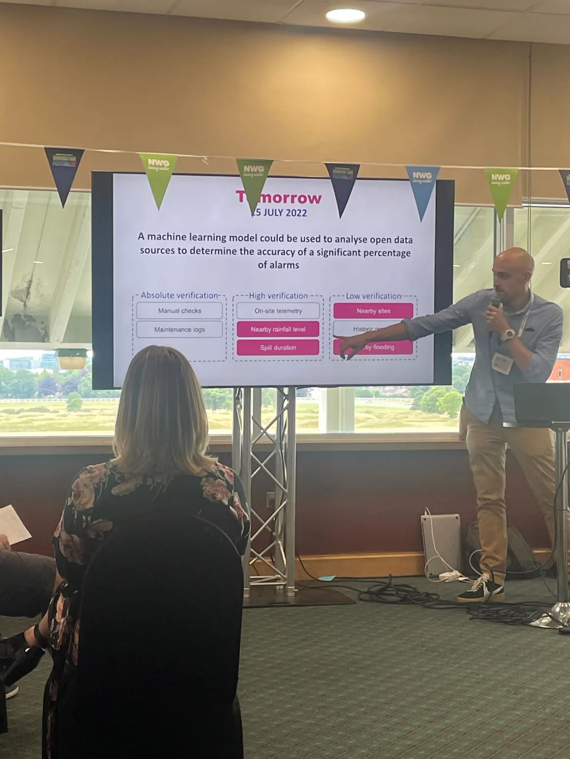 John Haynes presenting the spill prediction proof of concept on stage at the NWG Innovation Festival, with the three-tier verification slide visible